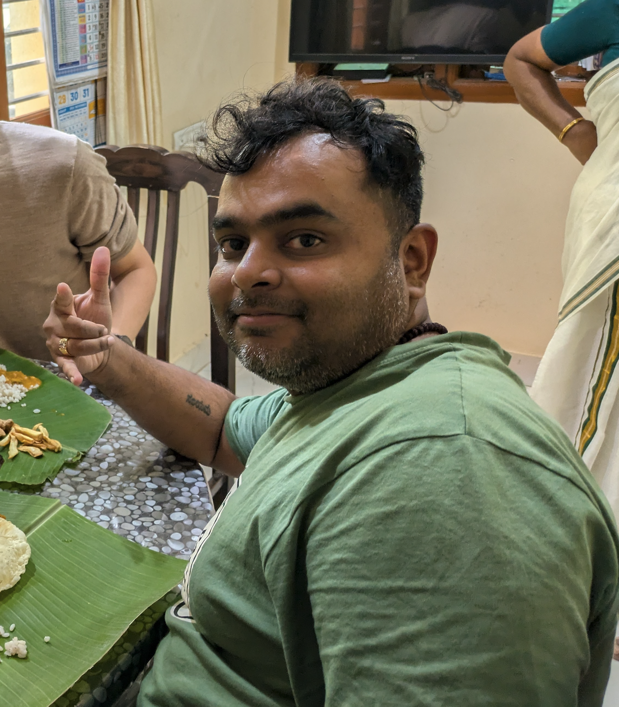 Nani looking back at the camera with a grin, mid-meal, banana-leaf plates on the table.